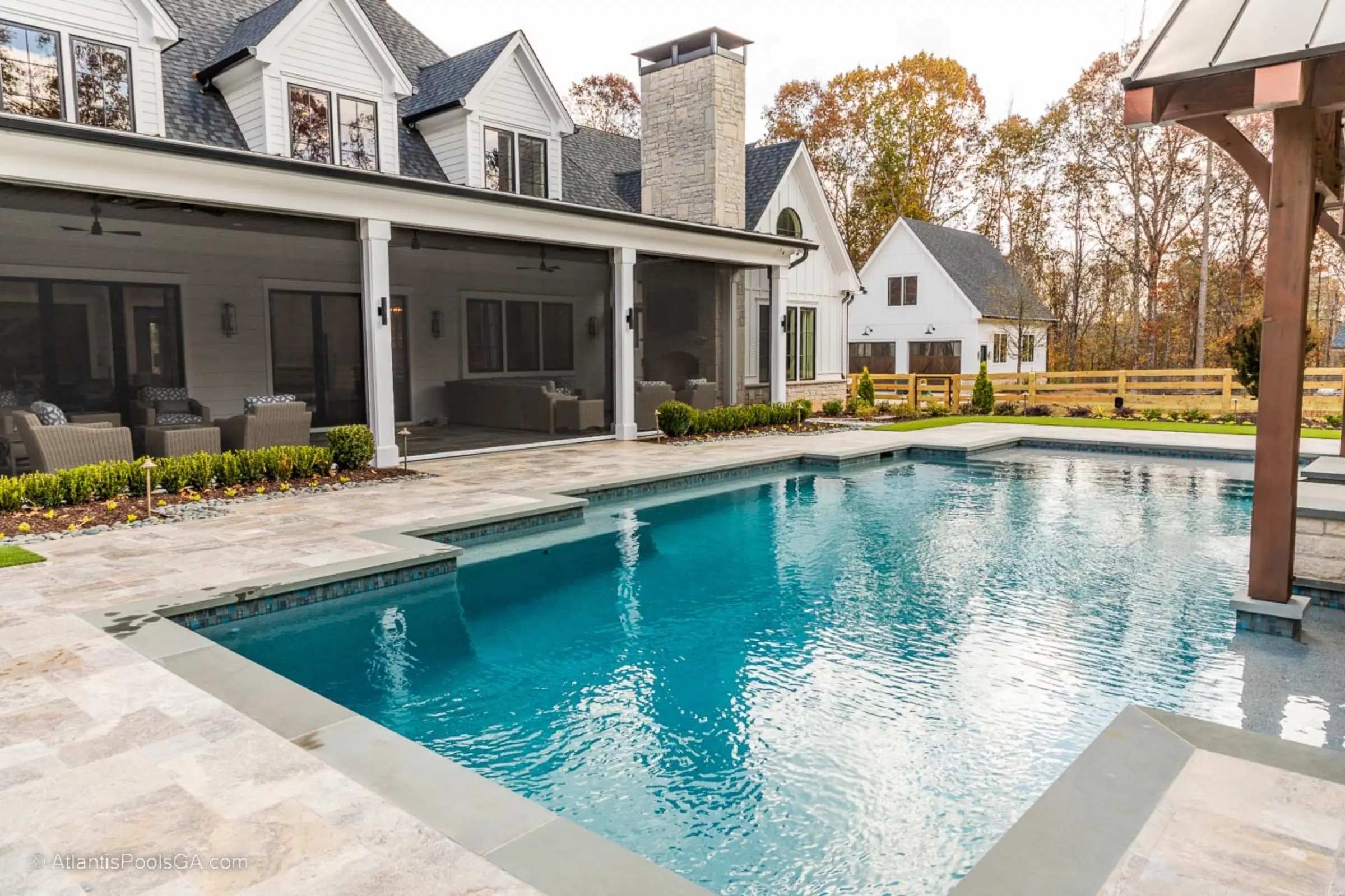 A linear pool with tanning shelf beside a modern farmhouse and covered patio, built by Atlantis Pools