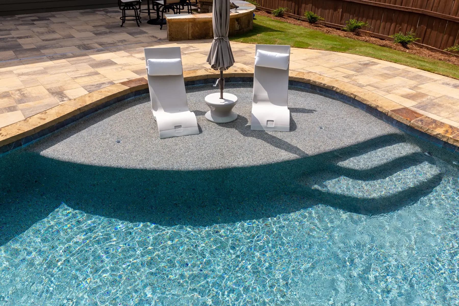 A submerged tanning ledge with lounge chairs and an umbrella, built into a freeform gunite pool