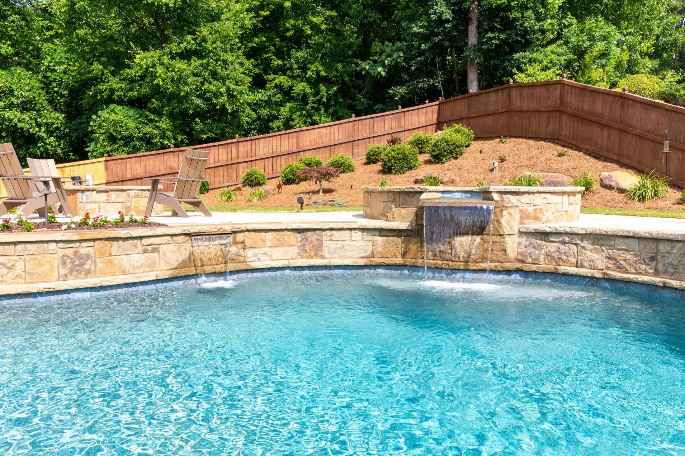 A freeform pool with a stone waterfall feature spilling into the water among mature trees.