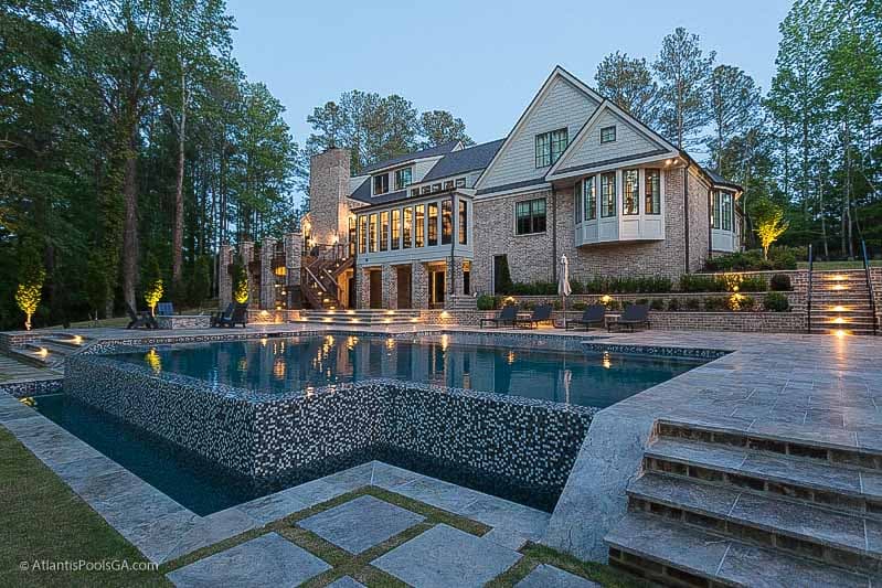 A geometric pool at twilight behind a stone and shingle home