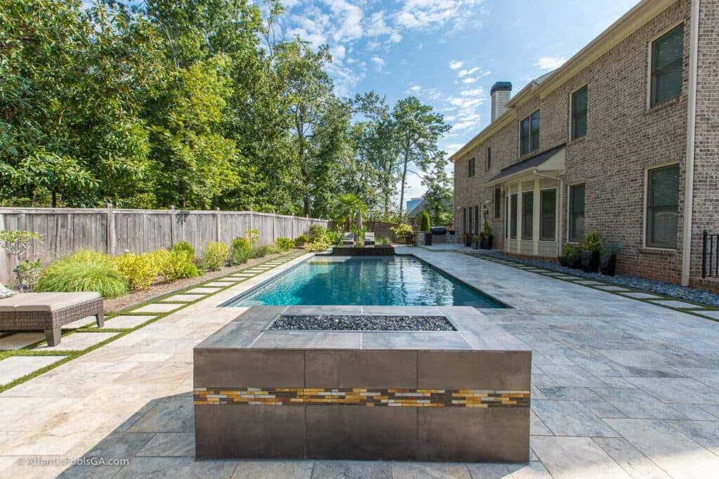 A rectangular pool and raised spa set beside a brick home, with a paved deck and planted border.