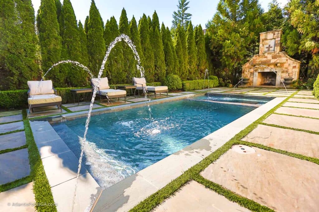 Deck jets arcing into a linear pool beside an outdoor fireplace, the kind of water features and finishes added in Atlantis renovation work