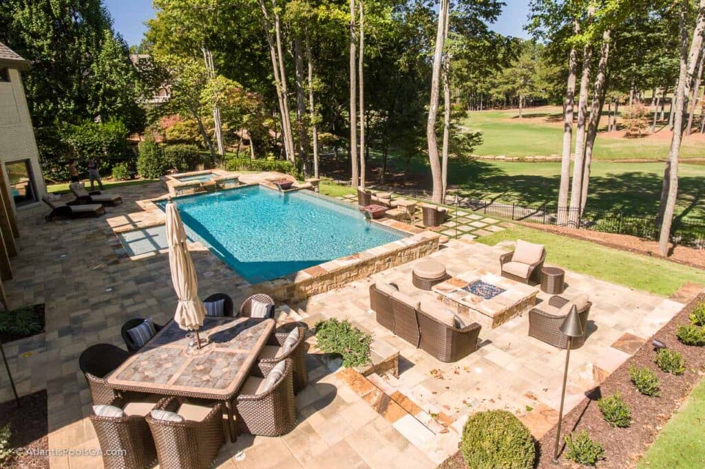 A long rectangular pool and outdoor dining terrace beside a wooded fairway