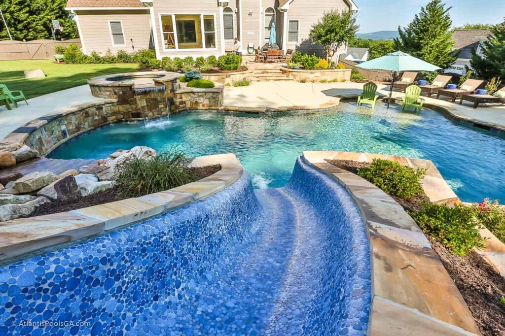 A freeform pool with a raised tiled spillway, planted stone, and a broad entertaining terrace