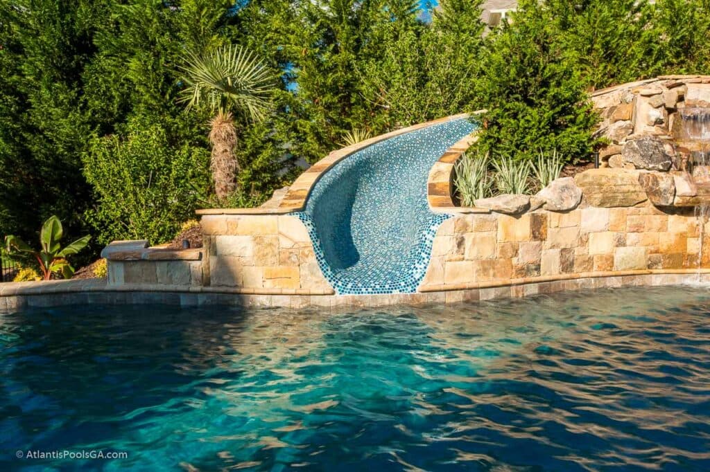 A curved pool slide dropping through stonework into a wooded pool