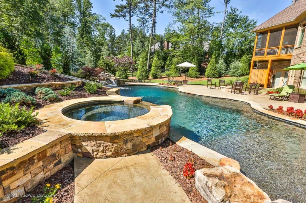 A stone-edged spa flowing into a pool beside a wooded garden