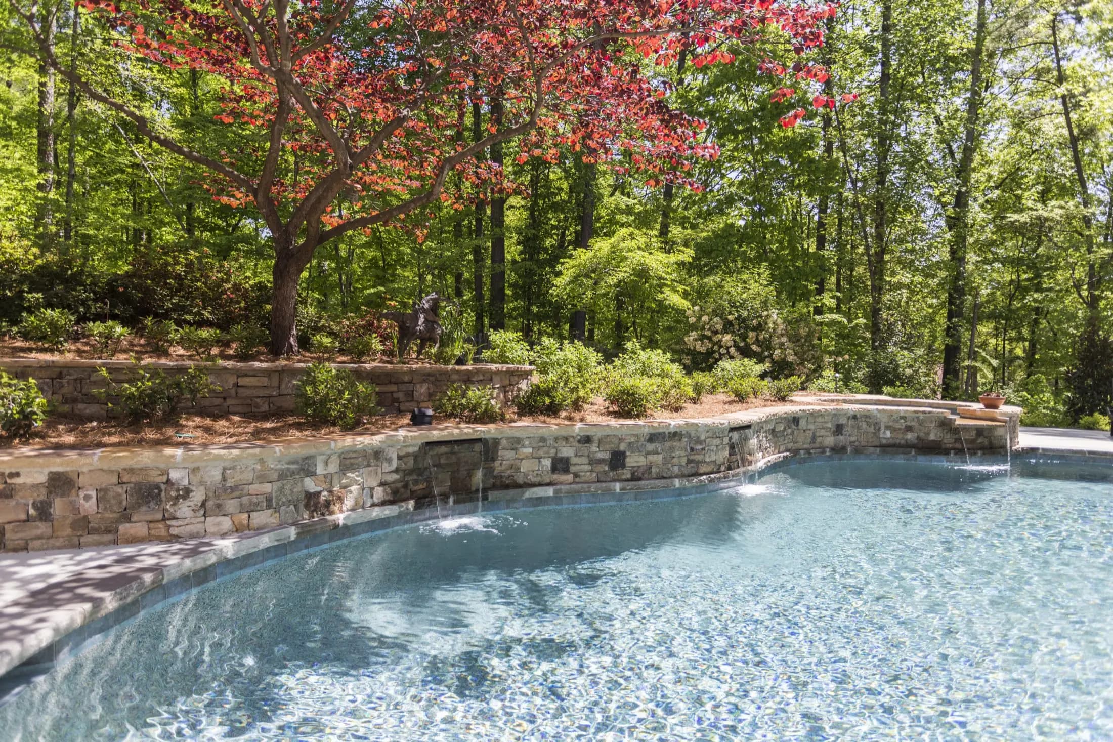 The Starke pool in Johns Creek, with a stone waterfall feature set beneath a maple tree